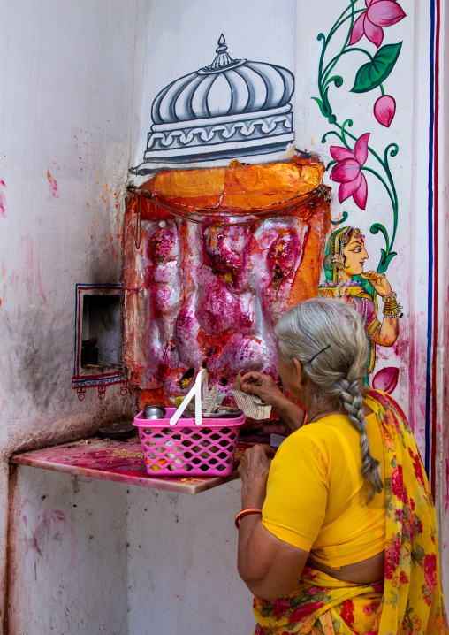 Indian woman praying in a temple decorated with murals depicting flowers, Rajasthan, Udaipur, India