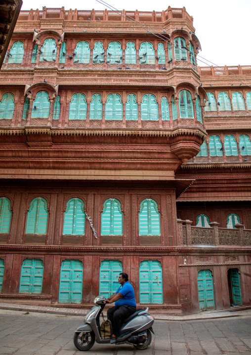 Indian man riding a scooter in front of a beautiful haveli in the old city, Rajasthan, Bikaner, India