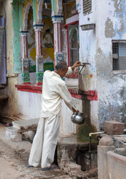 Indian man collecting water in the street during the heat wave, Rajasthan, Bundi, India