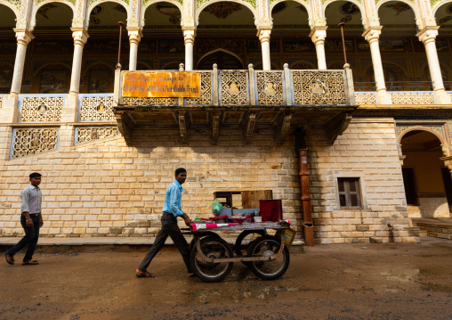 Indian man pushing a cart in front of an old historic haveli, Rajasthan, Nawalgarh, India