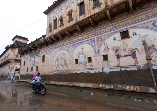 Indian people riding a motorbike and passing by an old historic haveli, Rajasthan, Nawalgarh, India