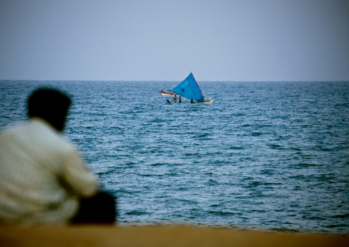 Man Sitting At Pondicherry Waterfront Looking At Fishermen On Their Boat, India