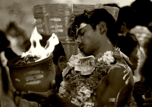 Young Man With Closed Eyes Covered With Traditional Painting And Offerings Holding A Jar On Fire During Fire Walking Ritual, Madurai, South India