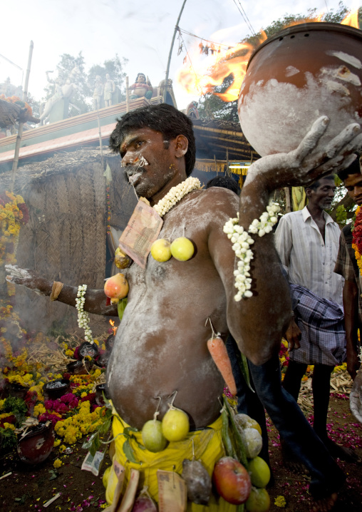 Indian Man Covered With Ashes Wearing Offerings Hooked On His Body And Holding A Jar On Fire Ready For Fire Walking Ritual, Madurai, South India