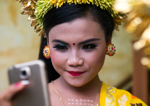A Teenager Girl In Traditional  Costume Using Her Mobile Phone As A Mirror  Before A Tooth Filing Ceremony