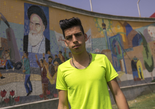 Young man with western haircut in front of ayatollah khomeini poster, Shemiranat county, Tehran, Iran