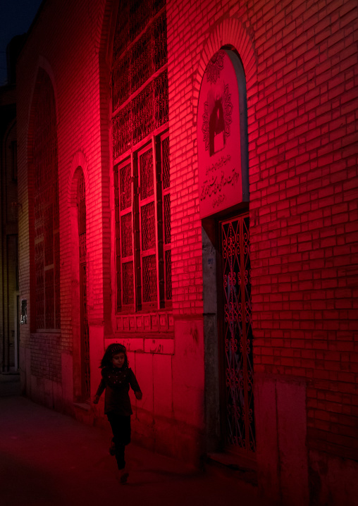Iranian girl running in a street illuminated with red light for Muharram to commemorate the martyrdom anniversary of Hussein, Isfahan Province, Isfahan, Iran