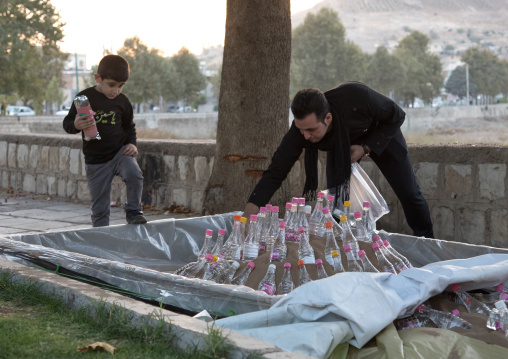 A father and his son preparing a mud pond with rose water bottles for the Kharrah Mali ritual during the Ashura ceremony, Lorestan Province, Khorramabad, Iran