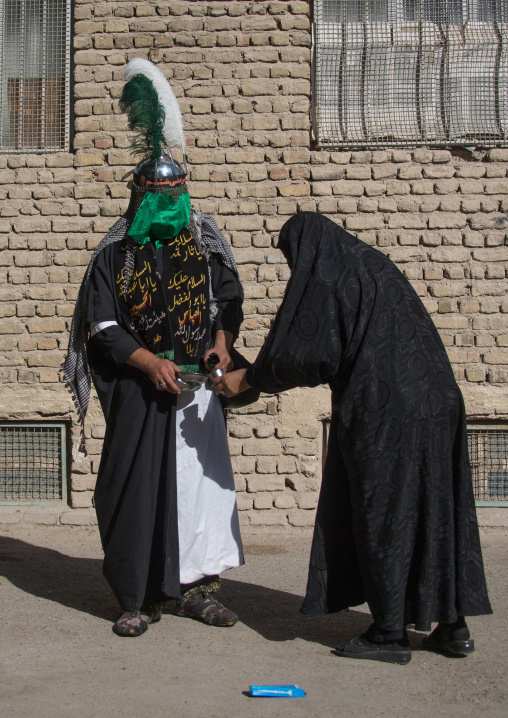 A Man dressed as Imam Hussein gives water to a woman on Tasua during the Chehel Manbar ceremony one day before Ashura, Lorestan Province, Khorramabad, Iran