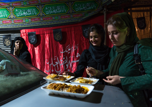 Women eating nazri charity food given during Muharram on a car hood, Central County, Theran, Iran