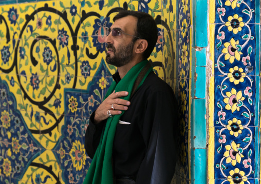 Shiite man praying in front of colorful faience tiles at Shrine of sultan Ali, Kashan County, Mashhad-e Ardahal, Iran
