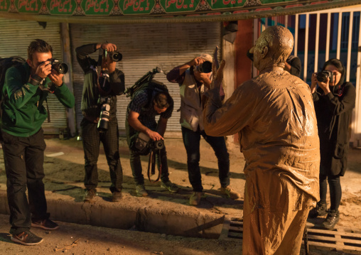 Photographers taking pictures of an iranian shiite muslim man who rubbed mud on his body during the Kharrah Mali ritual to mark the Ashura ceremony, Lorestan Province, Khorramabad, Iran