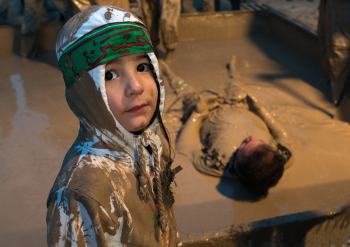 An iranian shiite muslim child in front of a mud pond while his father takes part in the Kharrah Mali ritual during the Ashura ceremony, Lorestan Province, Khorramabad, Iran