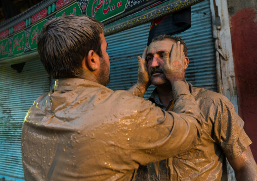 Iranian shiite muslim man rubbing mud on the face of a friend during the Kharrah Mali ritual to mark the Ashura day, Lorestan Province, Khorramabad, Iran
