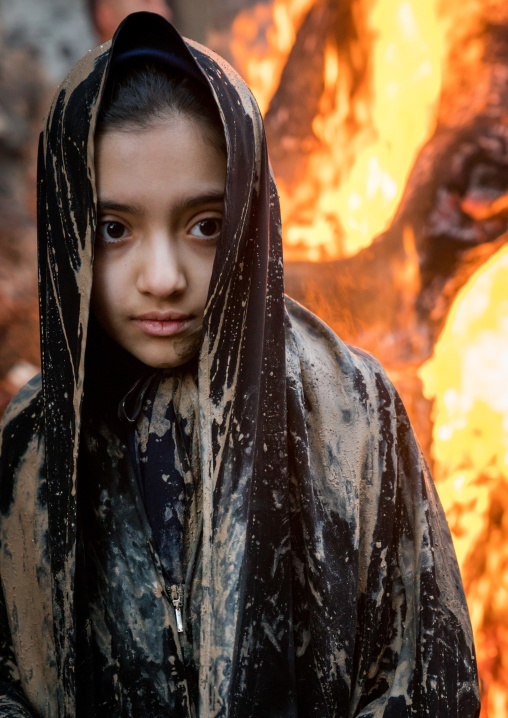 An Iranian shiite muslim girl stands in front a bonfire after rubbing mud on her chador during the Kharrah Mali ritual to mark the Ashura day, Lorestan Province, Khorramabad, Iran