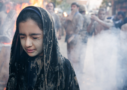 An Iranian shiite muslim girl with closed eyes stands in front a bonfire after rubbing mud on her chador during the Kharrah Mali ritual to mark the Ashura day, Lorestan Province, Khorramabad,