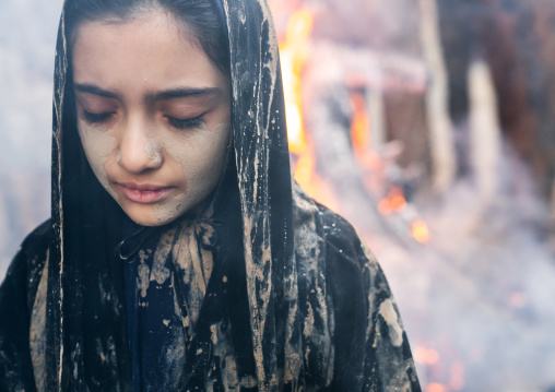 An Iranian shiite muslim girl with closed eyes stands in front a bonfire after rubbing mud on her chador during the Kharrah Mali ritual to mark the Ashura day, Lorestan Province, Khorramabad,