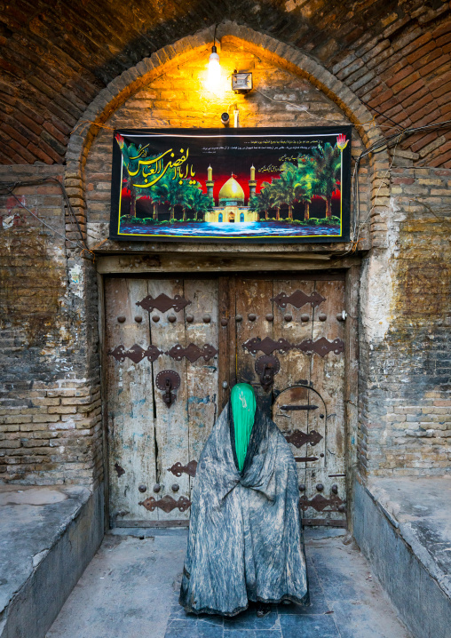 Iranian shiite muslim woman standing in front of an old wooden door after rubbing mud on her chador during the Kharrah Mali ritual to mark the Ashura ceremony, Lorestan Province, Khorramabad,