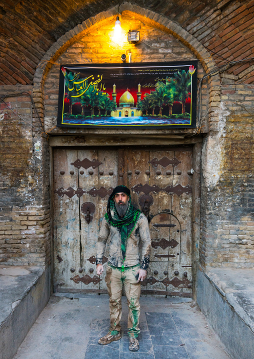 Iranian shiite muslim man standing in front of an old wooden door after rubbing mud on his clothes during the Kharrah Mali ritual to mark the Ashura ceremony, Lorestan Province, Khorramabad, 