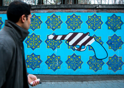 man passing in front of anti-american mural propoganda on the wall of the former united states embassy, Central district, Tehran, Iran