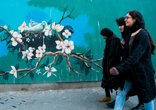women passing in front of anti-american mural propoganda on the wall of the former united states embassy, Central district, Tehran, Iran
