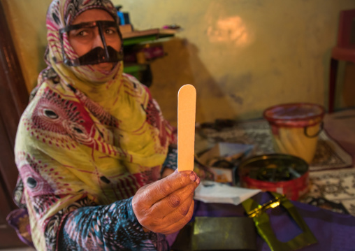 a bandari woman with a traditional mask and showing an ice cream short stick she uses for the mask, Qeshm Island, Salakh, Iran