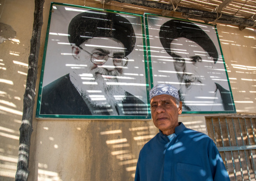 old bandari sailor in front of khameini and khomeini portraits in a house, Hormozgan, Bandar-e Kong, Iran