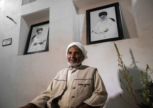 old bandari sailor in front of khameini and khomeini portraits in a house, Hormozgan, Bandar-e Kong, Iran