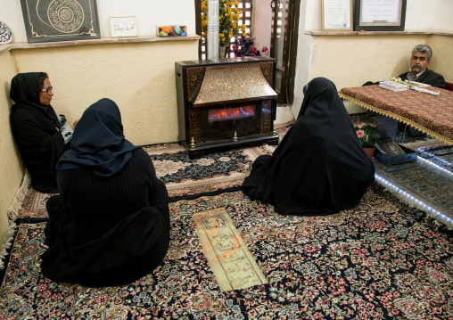 women in black chadors resting in front of a fireplace inside three domes moshtaghie, Central County, Kerman, Iran