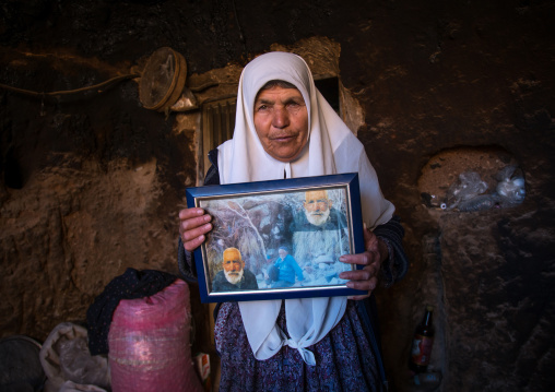 old widow woman in her troglodyte house showing the pictures of her dead husband and father, Kerman province, Meymand, Iran