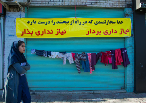 woman passing in front of a wall of kindness created to give clothes for free to poor people, Central County, Yazd, Iran