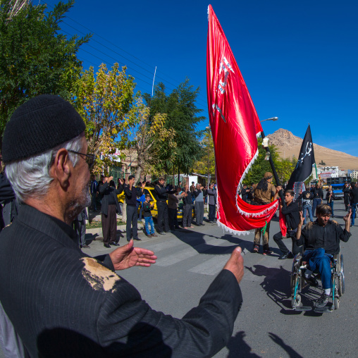 Man In Wheelchair In Front Of A Red Flag Celebrating Ashura, The Day Of The Death Of Imam Hussein, Kurdistan Province, Bijar, Iran
