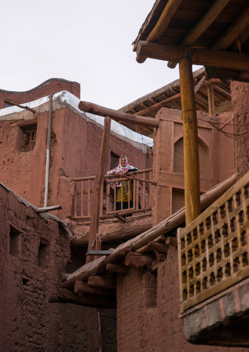 Iranian Woman Standing At The Balcony Of An Ancient Building In Zoroastrian Village, Isfahan Province, Abyaneh, Iran