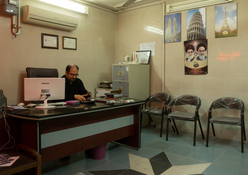 Man Working With A Computer In A Travel Agency Office With Khomeini Picture On The Wall, Isfahan Province, Kashan, Iran