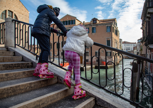 Mother and girl with  roller-skates on a stair in the old town, Veneto, Venice, Italia