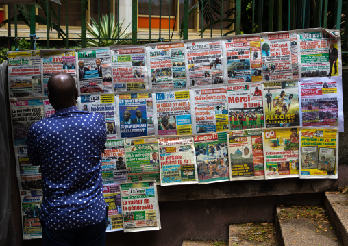 African man reading newspapers displayed on a market stall, Région des Lagunes, Abidjan, Ivory Coast