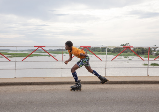 African boy roller skating on the bridge over Ouladine lagoon, Sud-Comoé, Grand-Bassam, Ivory Coast
