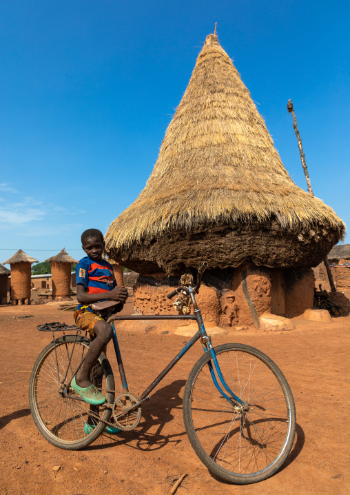 African boy with a bicycle in front of a Senufo fetish house whose roof gets a new layer every year, Savanes district, Niofoin, Ivory Coast