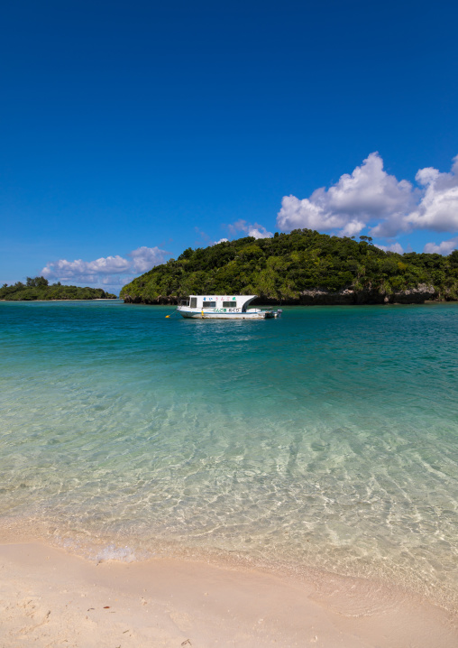 Glass bottom boat in the tropical lagoon beach with clear blue water and white sand surrounded by lush greenery in Kabira bay, Yaeyama Islands, Ishigaki, Japan