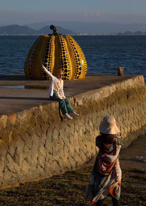 Tourist taking pictures of the yellow pumpkin by Yayoi Kusama on pier at sea, Seto Inland Sea, Naoshima, Japan