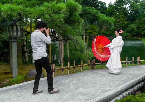 Japanese photographer taking picture of a woman with oil paper umbrella in Kenroku-en garden, Ishikawa Prefecture, Kanazawa, Japan