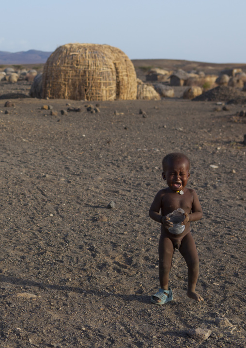 Baby crying in front of grass huts in el molo tribe village, Turkana lake, Loiyangalani, Kenya
