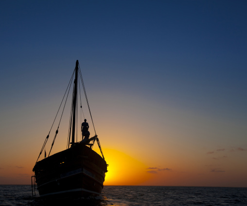 Man standing at the prow of a dhow in the sunset, Lamu county, Lamu, Kenya