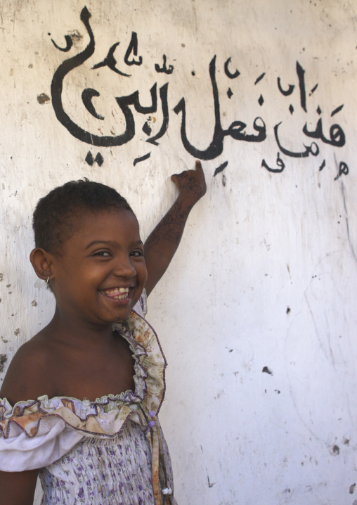 Portrait of a smiling swahili girl in front of arabic calligraphy on a wall, Lamu County, Lamu, Kenya