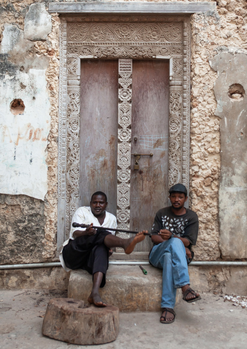 Kenyan men in front of a carved wooden front door, Lamu County, Lamu, Kenya