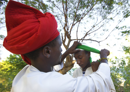 Muslim man putting a turban on another man head during Maulid festival, Lamu County, Lamu, Kenya