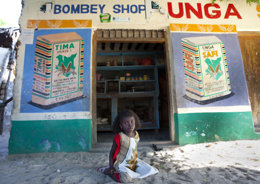 Young girl sitting in the sandy street outside a shop, Lamu County, Lamu, Kenya