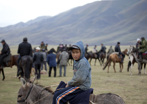 Young Boy With Cap Riding A Donkey In The Middle Of Adults Riding Horses, Saralasaz Jailoo, Kyrgyzstan