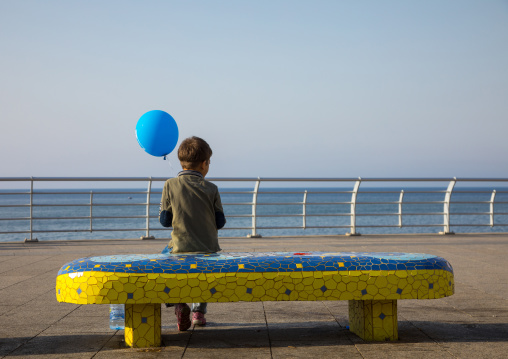 Boy sit on a bench with a balloon in the corniche, Beirut Governorate, Beirut, Lebanon