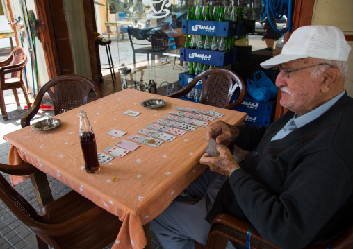 Old man playing cards alone at cafe table, North Governorate, Tripoli, Lebanon